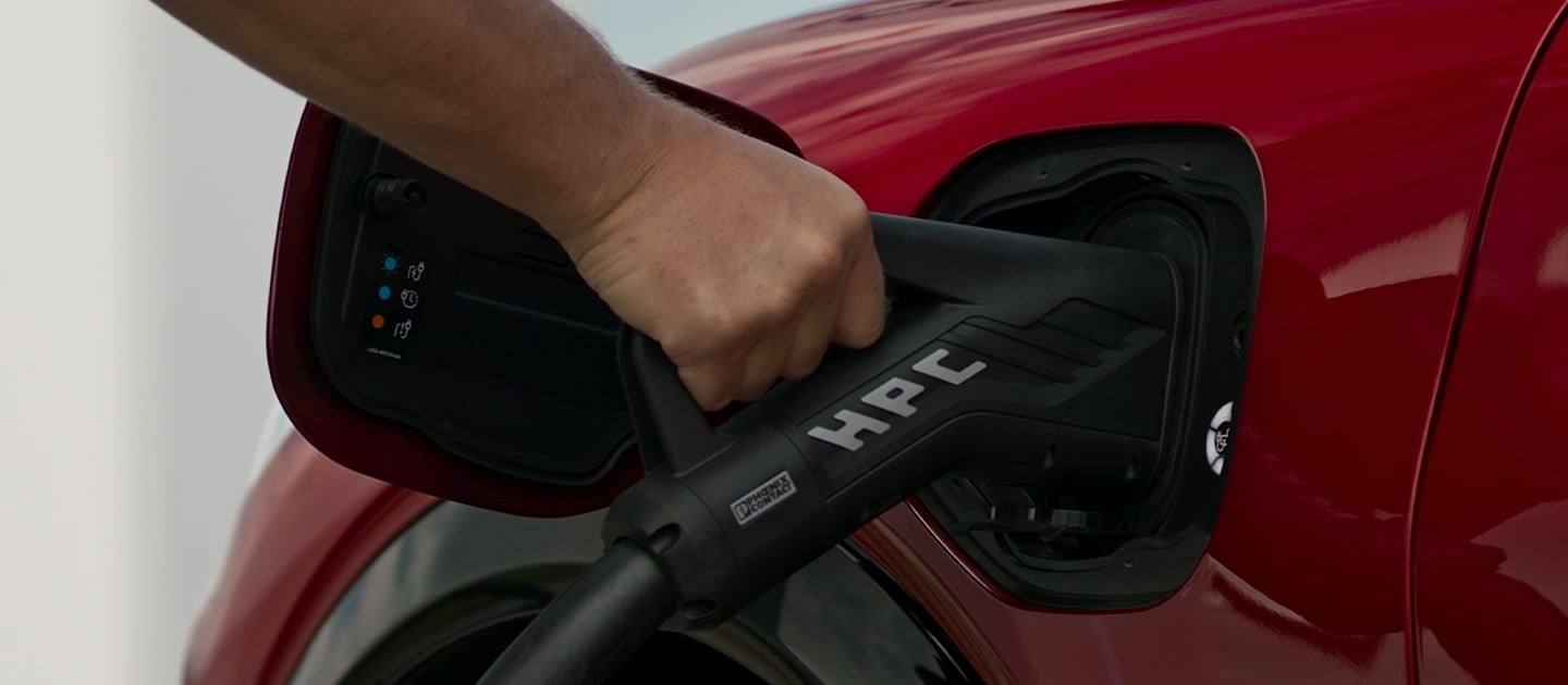 Lähikuva punaisesta Ford-täyssähköautosta kytkettynä pikalaturiin julkisella latausasemalla.