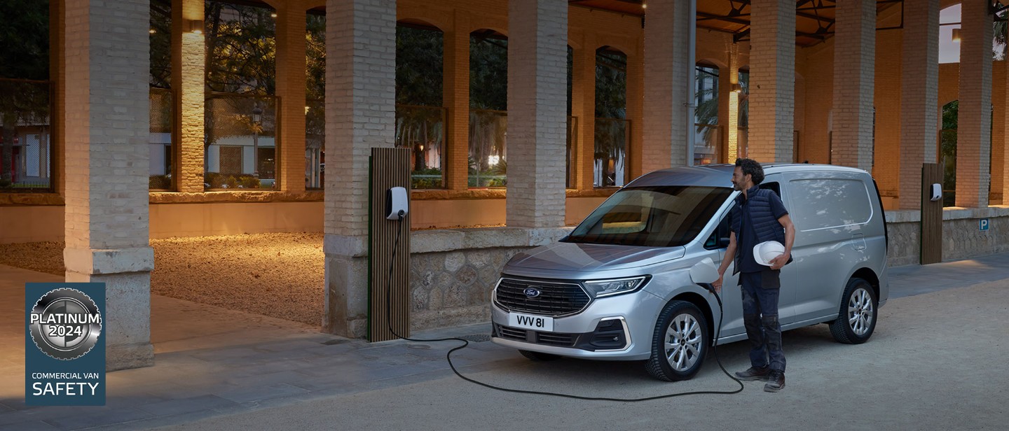 A man holding a hard hat plugs a wall box charging cable into All-New Ford Transit Connect in Stardust Silver. 